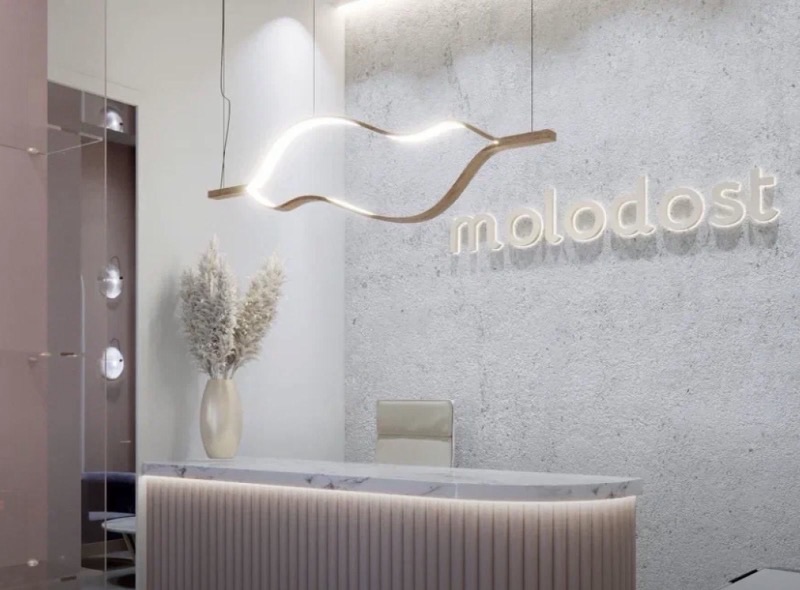 Рендер ресепшена клиники MOLODOST: изогнутая стойка, светильник волной, логотип на стене